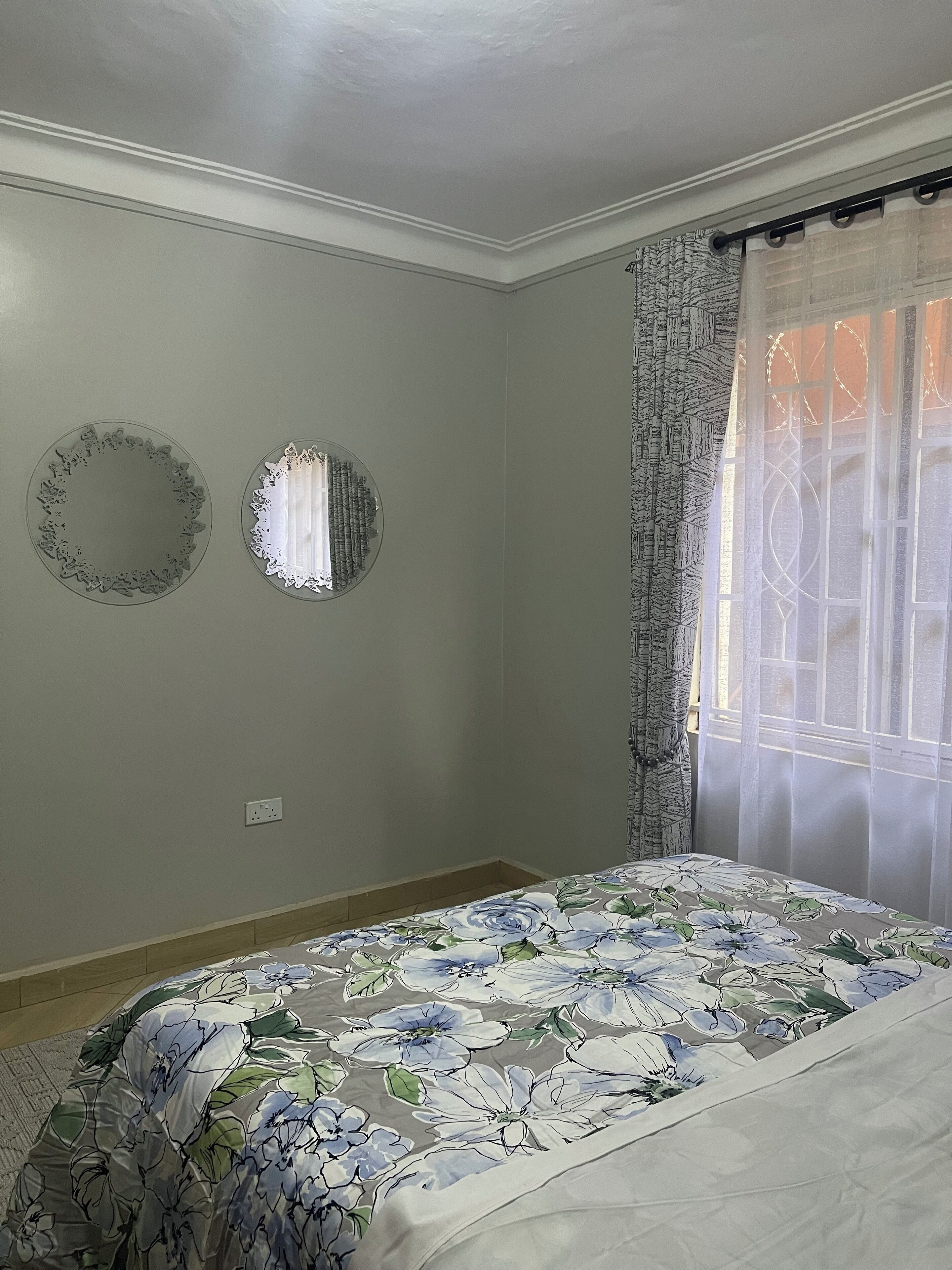 A bedroom with a bed, a wall-mounted mirror, and a window with curtains.