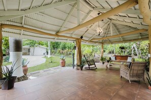 A covered patio area with tiled flooring, a wooden bench, a rocking chair, and potted plants.