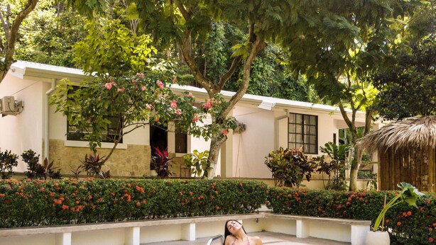 A woman relaxing by a pool with a thatched roof structure in the background. - Serene Jungle Bungalow at Mística Natural, Just Minutes to Stunning Beaches! (Puerto Viejo)