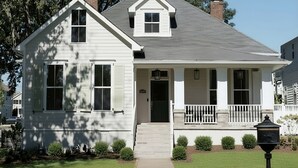 A two-story house with a front porch, a chimney, and a small front yard with bushes.