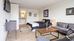 Un soggiorno moderno con un letto, un divano, un tavolino e una TV fissata alla parete.