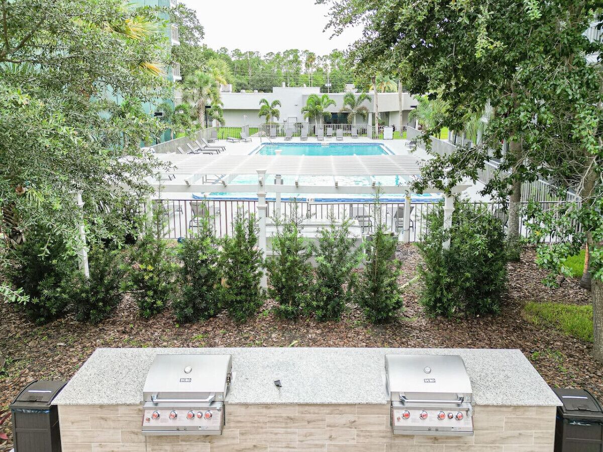Zona de piscina con estación de barbacoa y vista a un edificio con piscina.
