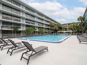 Ett hotell med en swimmingpool, solstolar och en byggnad i flera våningar med balkonger.