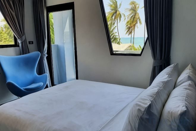 A bedroom with a bed, a window with a view of the beach, and a blue chair.