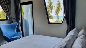 A bedroom with a bed, a blue chair, a window with a view of palm trees and the beach, and a door. - Stardust Boutique Hotel (Hua Hin)