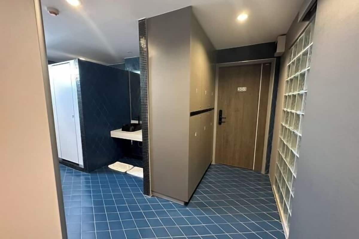 Ein Hotelzimmer mit blau gefliestem Boden, einem Kleiderschrank, einer Tür mit einer Nummer und einem Fenster mit Gittermuster.