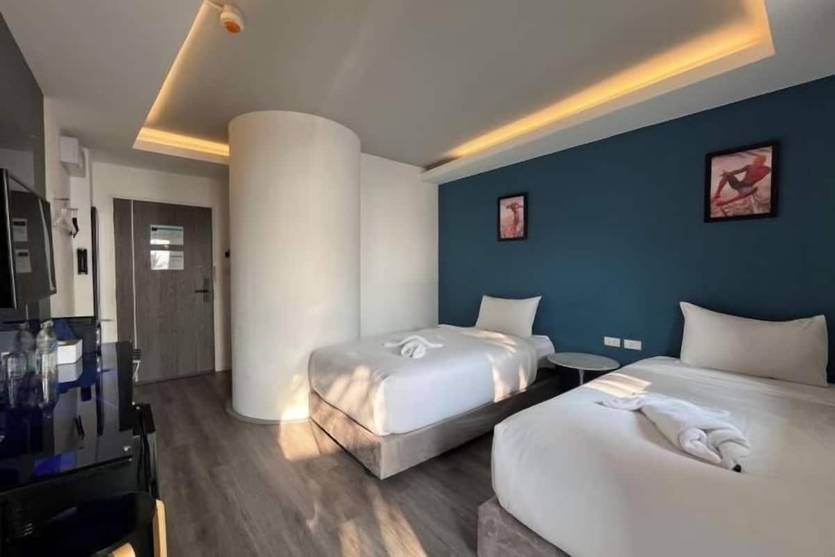 Ein Hotelzimmer mit zwei Betten, einem Fernseher, einem kleinen Tisch und einer blauen Akzentwand.