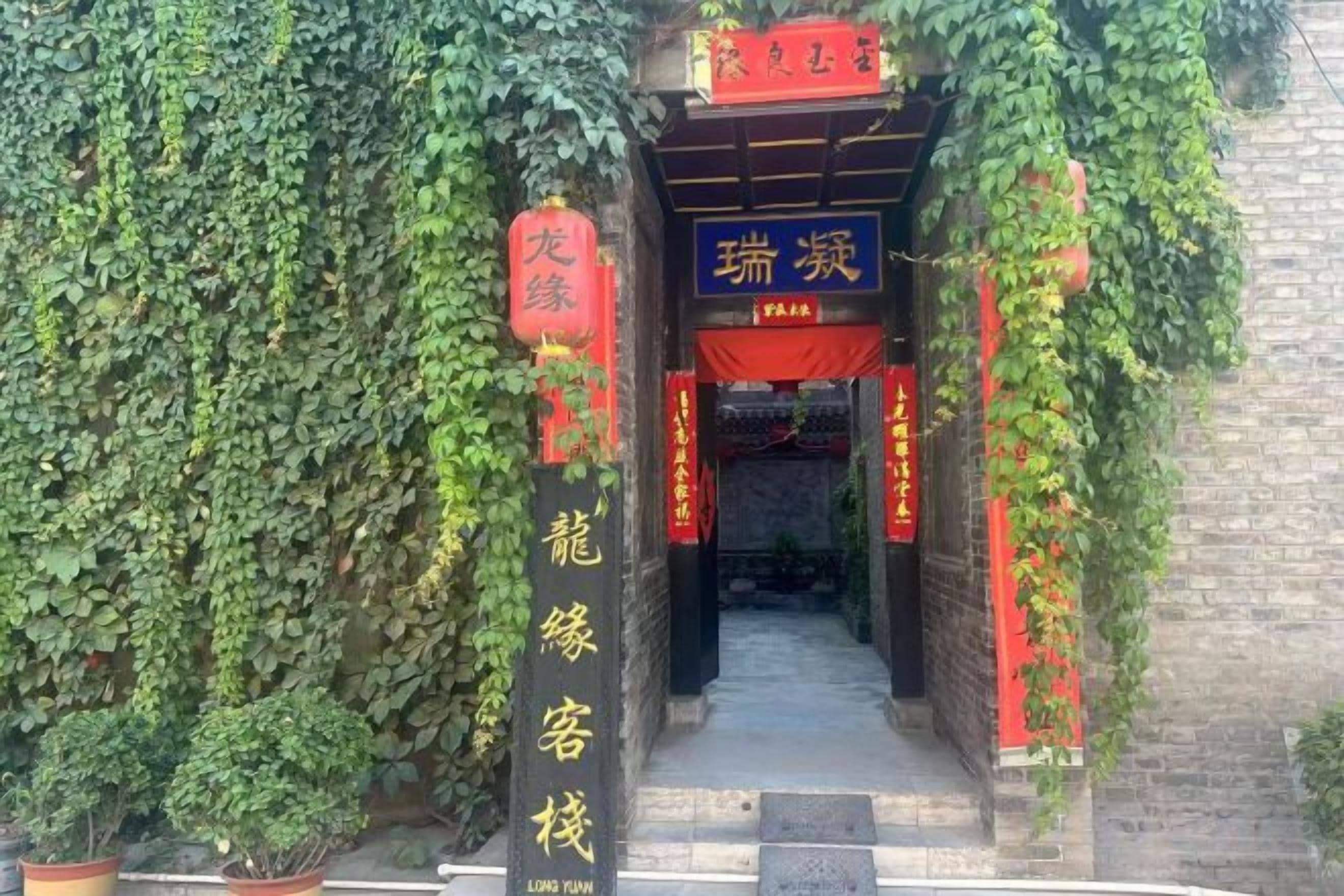 A traditional Chinese gate with red decorations and Chinese characters, leading to a building with a signboard.
