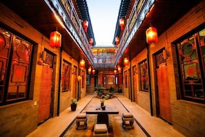 Un pasillo con arquitectura tradicional china, linternas y una mesa central con bancos.