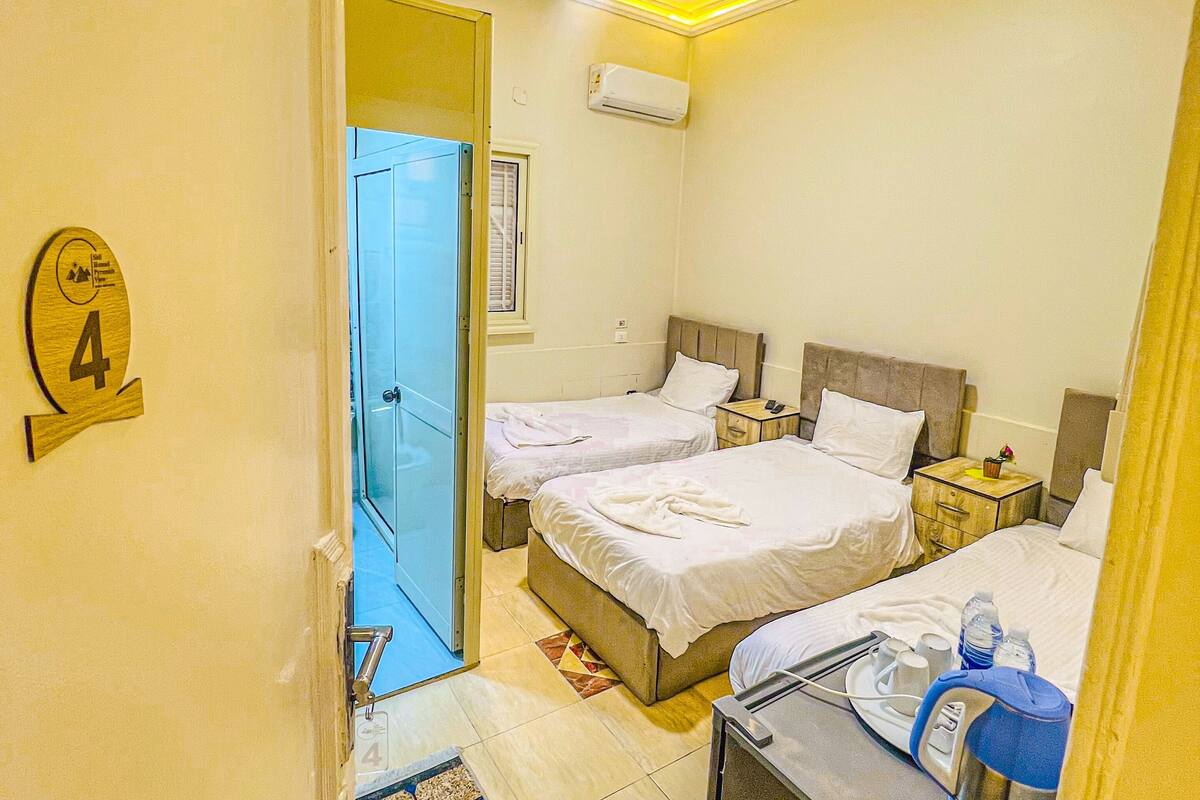 Habitación de hotel con dos camas, un escritorio con computadora, una mesita de noche con lámpara y un equipo de aire acondicionado en la pared.