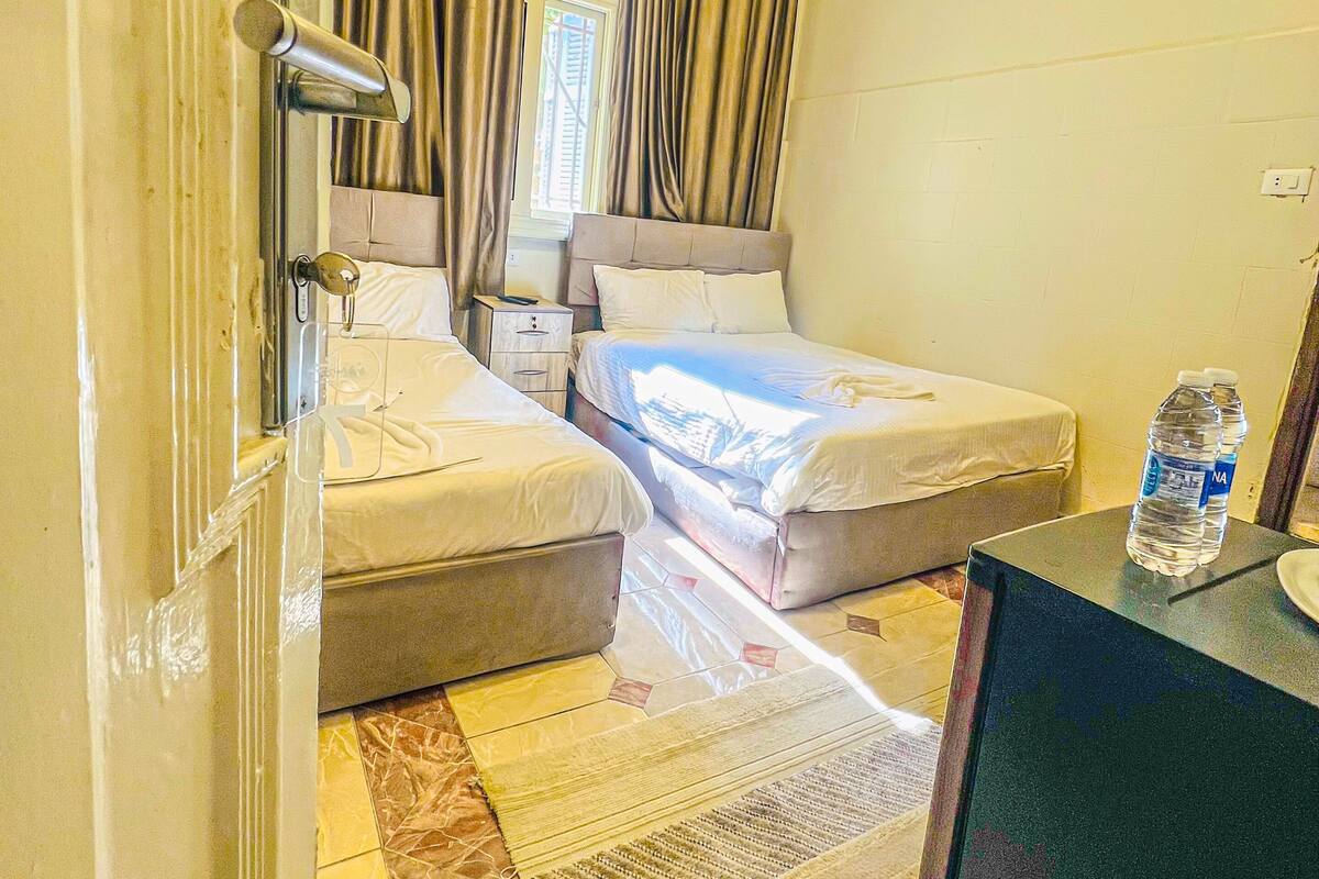 Habitación de hotel con dos camas, un escritorio pequeño, una botella de agua y vistas al exterior.
