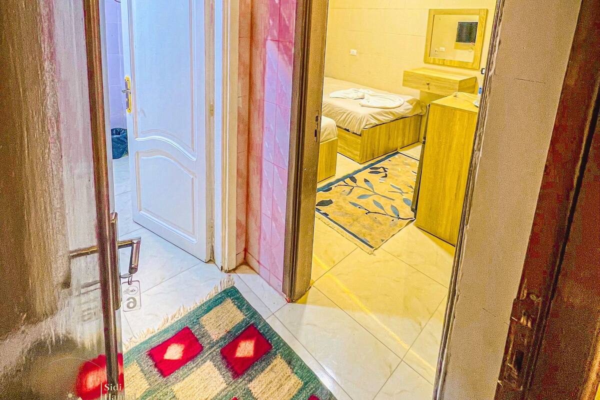 Un pasillo de hotel con alfombra estampada, una cama con cabecera de madera y un espejo en la pared.