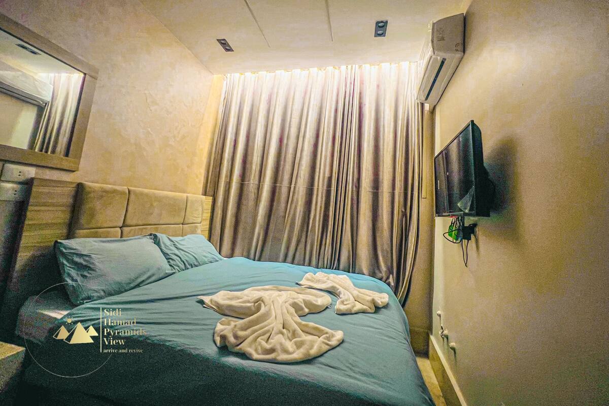 Habitación de hotel con cama, televisor montado en la pared y ventana con cortinas.