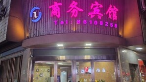 Un hotel con un letrero de neón en rosa y azul que muestra el nombre y el número de contacto.