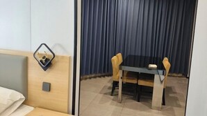 Habitación de hotel con cama, mesita de noche con espejo, pequeña mesa con sillas y ventana con cortinas.