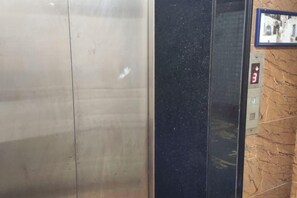 An elevator interior with a metallic finish and a control panel with a red button. - Jiuyuejiu Business Hotel (Tongxiang)