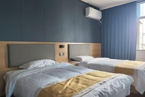 A hotel room with two beds, a wooden headboard, a wall-mounted air conditioner, and a window with blue curtains. - Jiuyuejiu Business Hotel (Tongxiang)