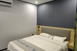 A hotel room with a bed, a nightstand, and a wall-mounted air conditioner. - Jiuyuejiu Business Hotel (Tongxiang)