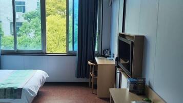 A hotel room with a bed, a desk with a chair, a television, and a window with curtains.