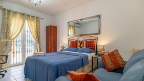 A bedroom with a bed, a sofa, a chair, a mirror, and curtains. - Cozy home in Sayalonga with WiFi (Sayalonga)