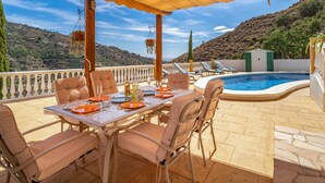 An outdoor patio with a table set for dining, surrounded by lounge chairs, and a swimming pool. - Cozy home in Sayalonga with WiFi (Sayalonga)