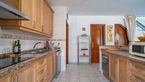A kitchen with wooden cabinets, granite countertops, a stainless steel range hood, a built-in dishwasher, and a glass shelving unit. - Cozy home in Sayalonga with WiFi (Sayalonga)