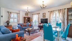 A living room with a sofa, coffee table, TV, and dining area with chairs and a glass table. - Cozy home in Sayalonga with WiFi (Sayalonga)