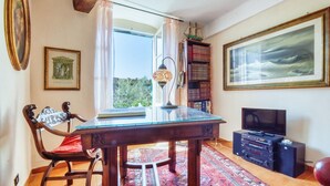 A room with a wooden table, a red chair, a bookshelf, a television, and a large framed painting. - 1 bedroom lovely home in Pieve Ligure (Pieve Ligure)
