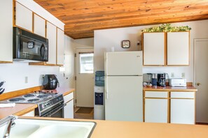 A compact kitchen with a microwave, stove, refrigerator, and a coffee maker.