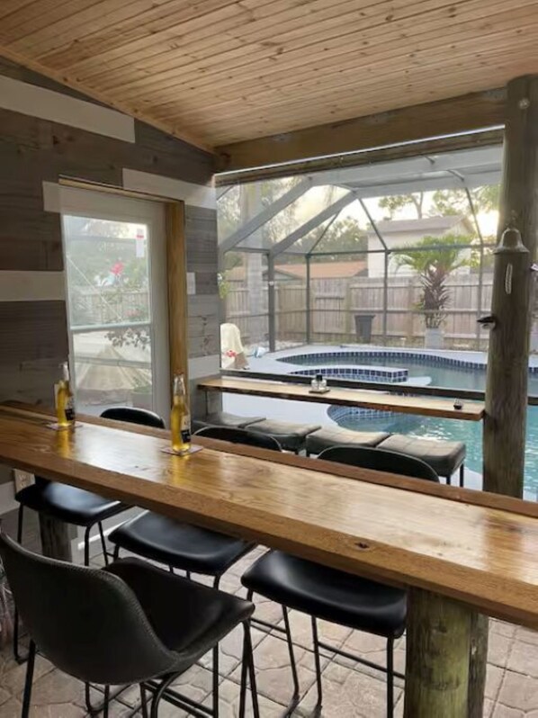 A bar area with a pool view, wooden ceiling, and outdoor seating.
