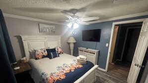 Ein Schlafzimmer mit einem Bett, einem Deckenventilator, einem Fernseher und einer Tür.
