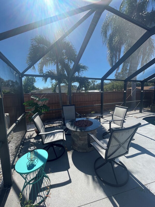 An outdoor patio with a fire pit, seating, and a view of the backyard.