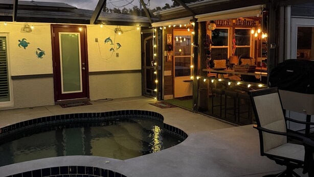 Ein Garten mit Pool, überdachter Terrasse und Esstisch.