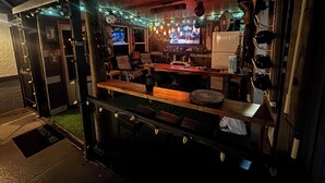 Eine Bar mit Holztresen, Barhocker und einem Fernsehbildschirm, der ein Sportereignis zeigt.