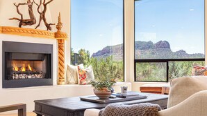Una sala de estar con chimenea, un ventanal con vistas a la montaña y un rincón de descanso acogedor.