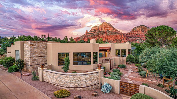 Una casa moderna con fachada de piedra, un jardín ajardinado y vistas a formaciones rocosas rojas.