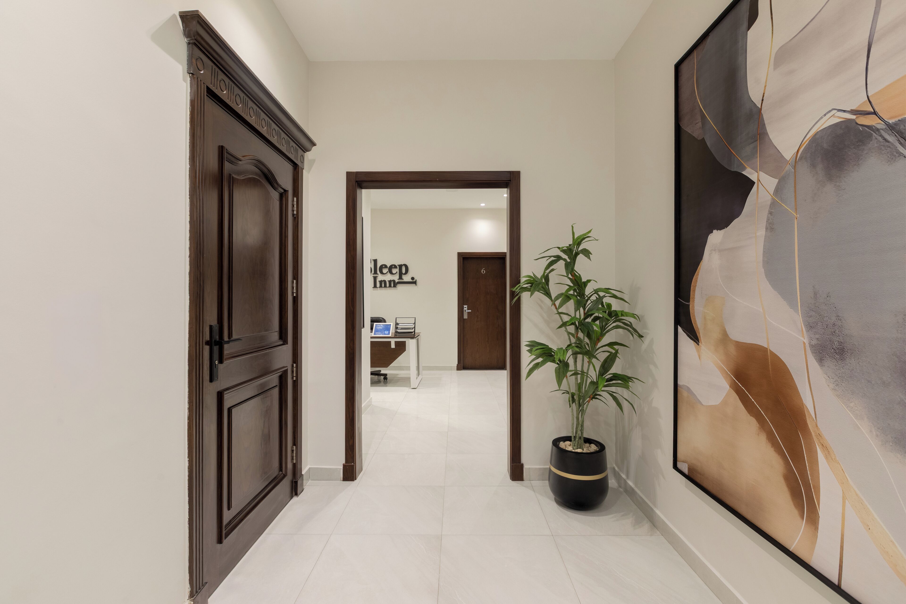A hallway with a wooden door, a reception desk, a large abstract painting, and a potted plant.