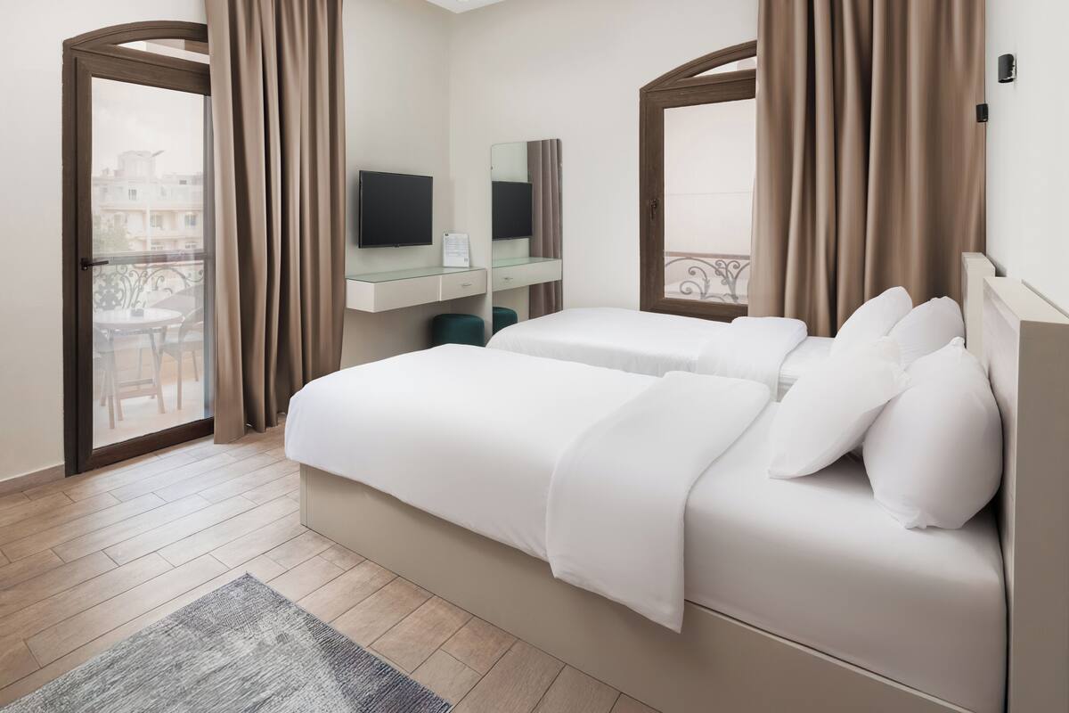 Habitación de hotel con cama, escritorio, televisión y vistas al balcón.