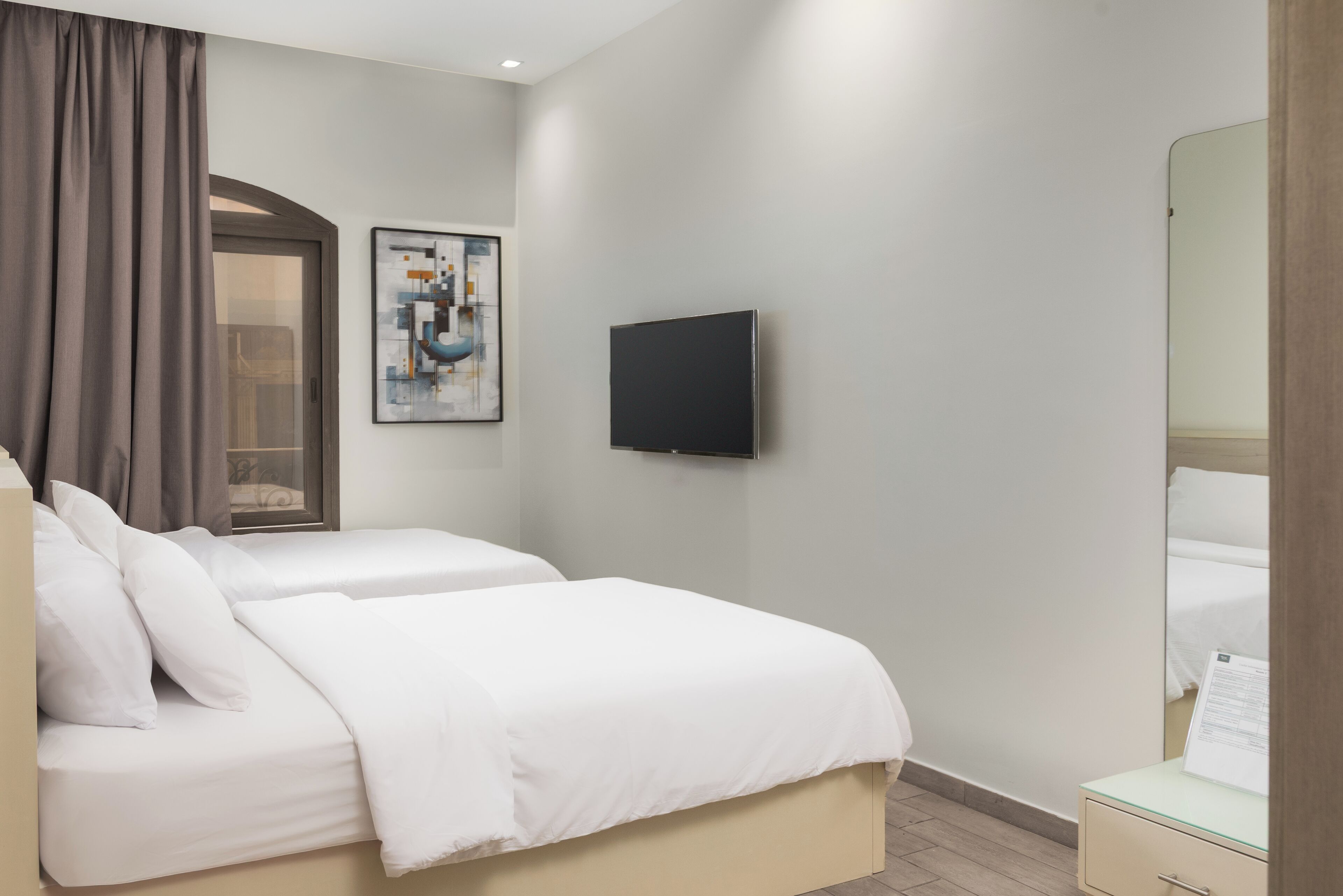 A hotel room with two beds, a flat-screen TV, a painting, and a mirror.