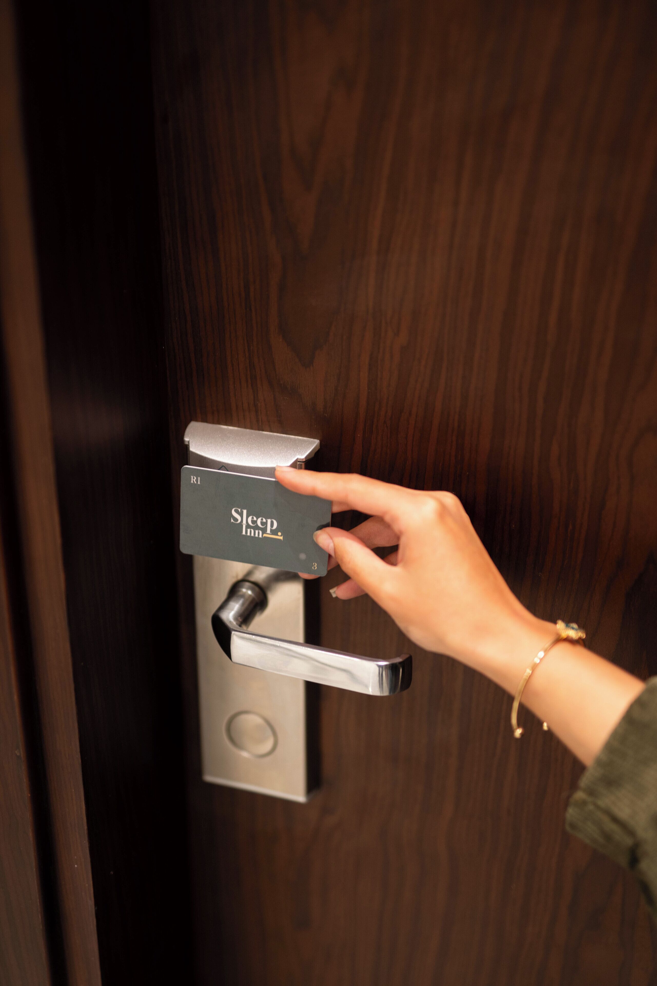 A hand operating a modern door lock with a card reader labeled "Sleep Inn."