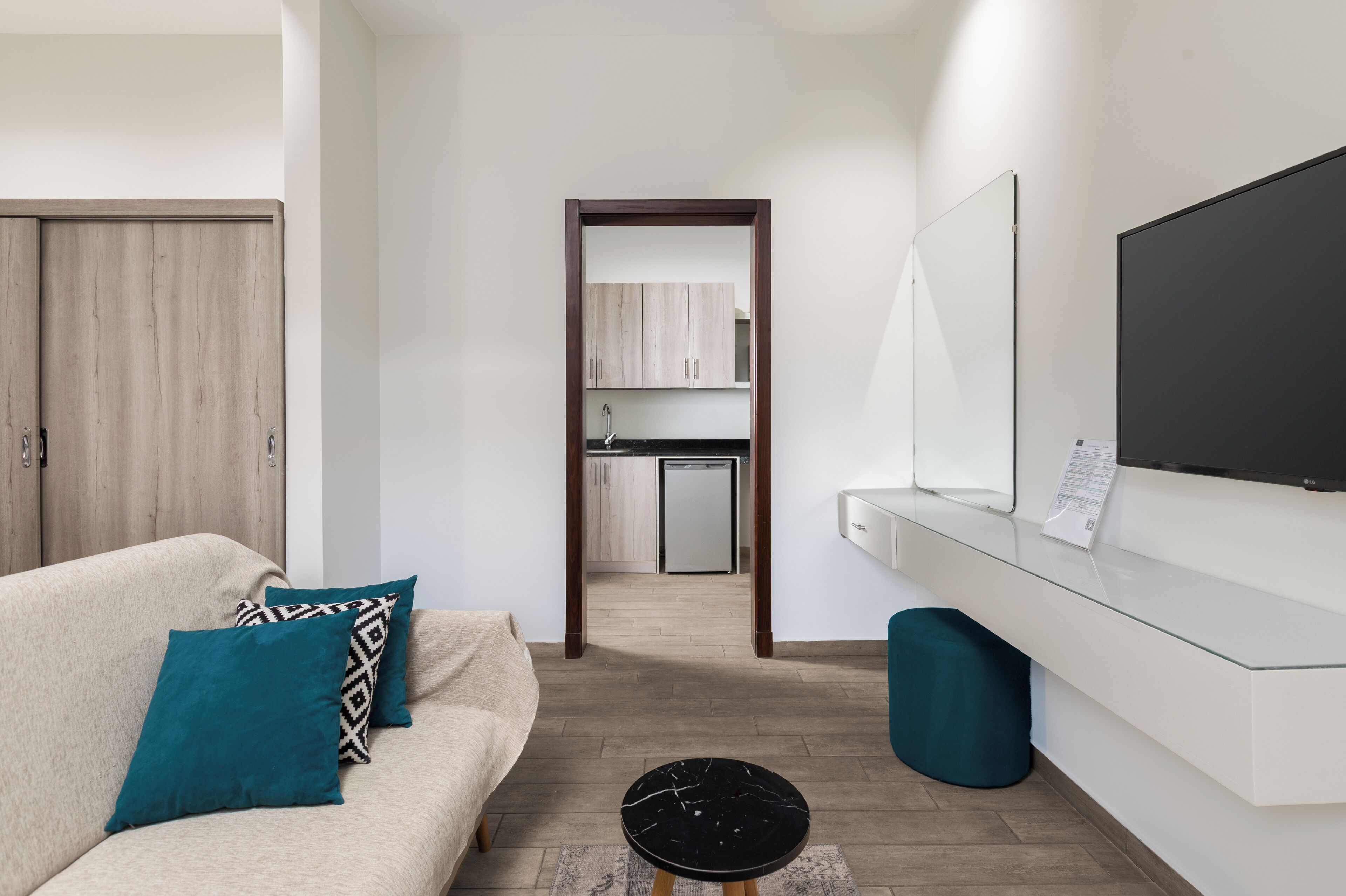 Una habitación de hotel moderna con sofá, televisor, una mesita y vistas al área de la cocina.