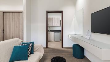 Una habitación de hotel moderna con sofá, televisor, una mesita y vistas al área de la cocina.