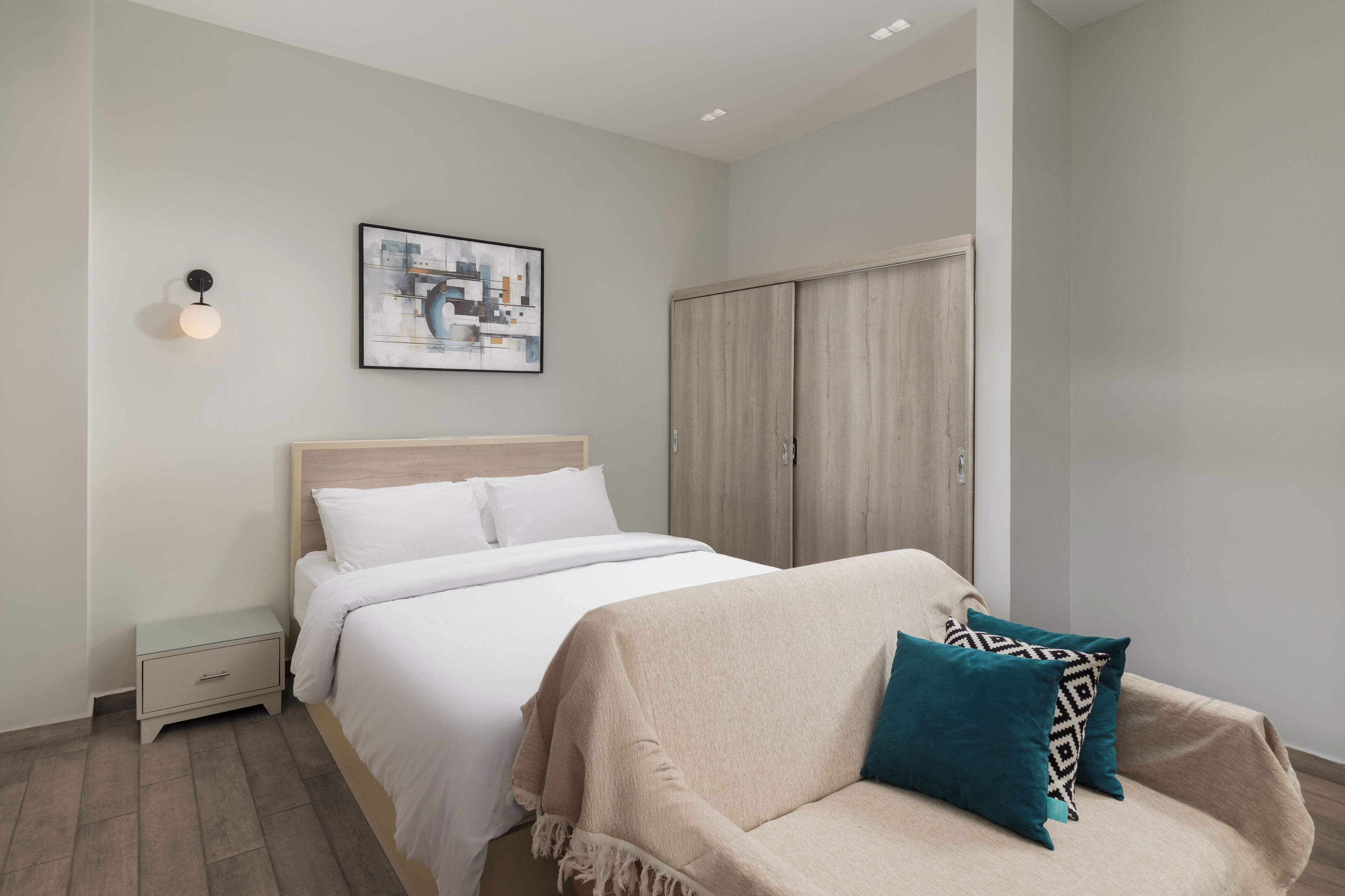 A bedroom with a bed, a nightstand, a sofa, a wardrobe, and a wall-mounted light fixture.