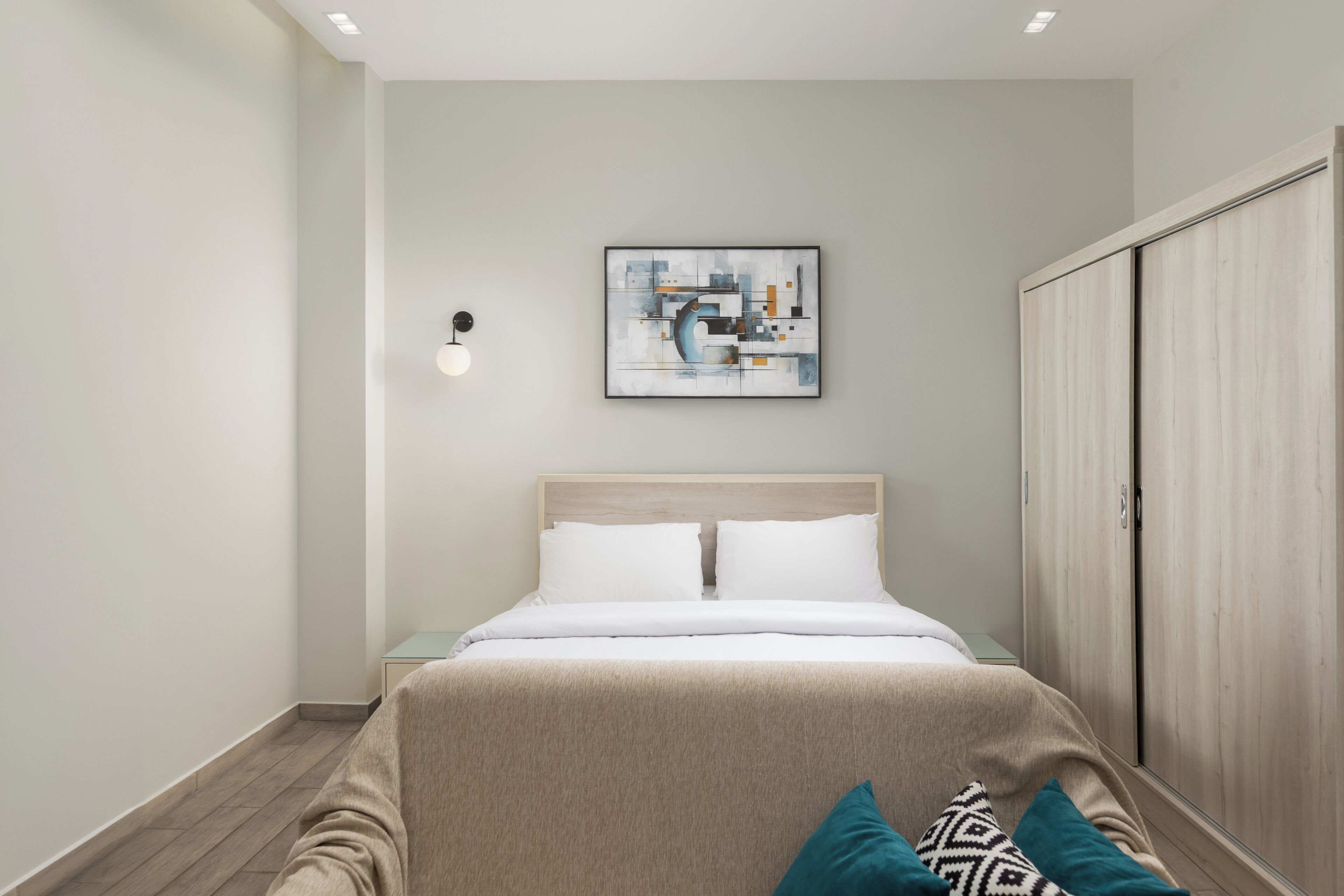 Ein modernes Schlafzimmer mit Bett, Nachttisch, Kleiderschrank und einem an der Wand hängenden abstrakten Gemälde.