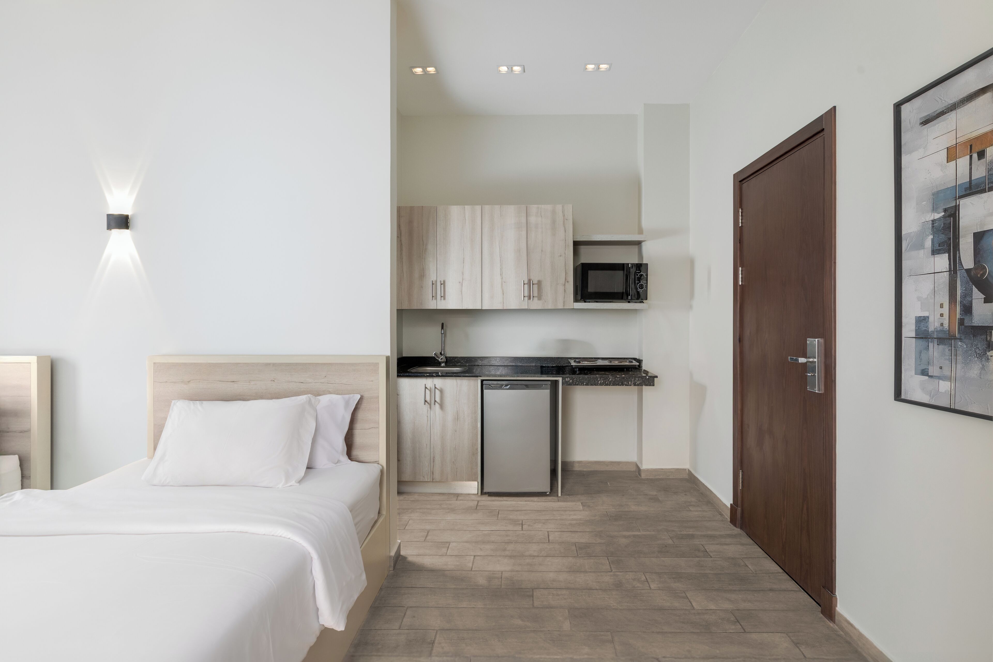 A bedroom with a bed, a small kitchenette with a microwave, and a wooden door.