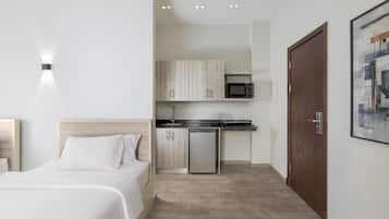 A bedroom with a bed, a small kitchenette with a microwave, and a wooden door.