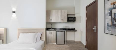 A bedroom with a bed, a small kitchenette with a microwave, and a wooden door.