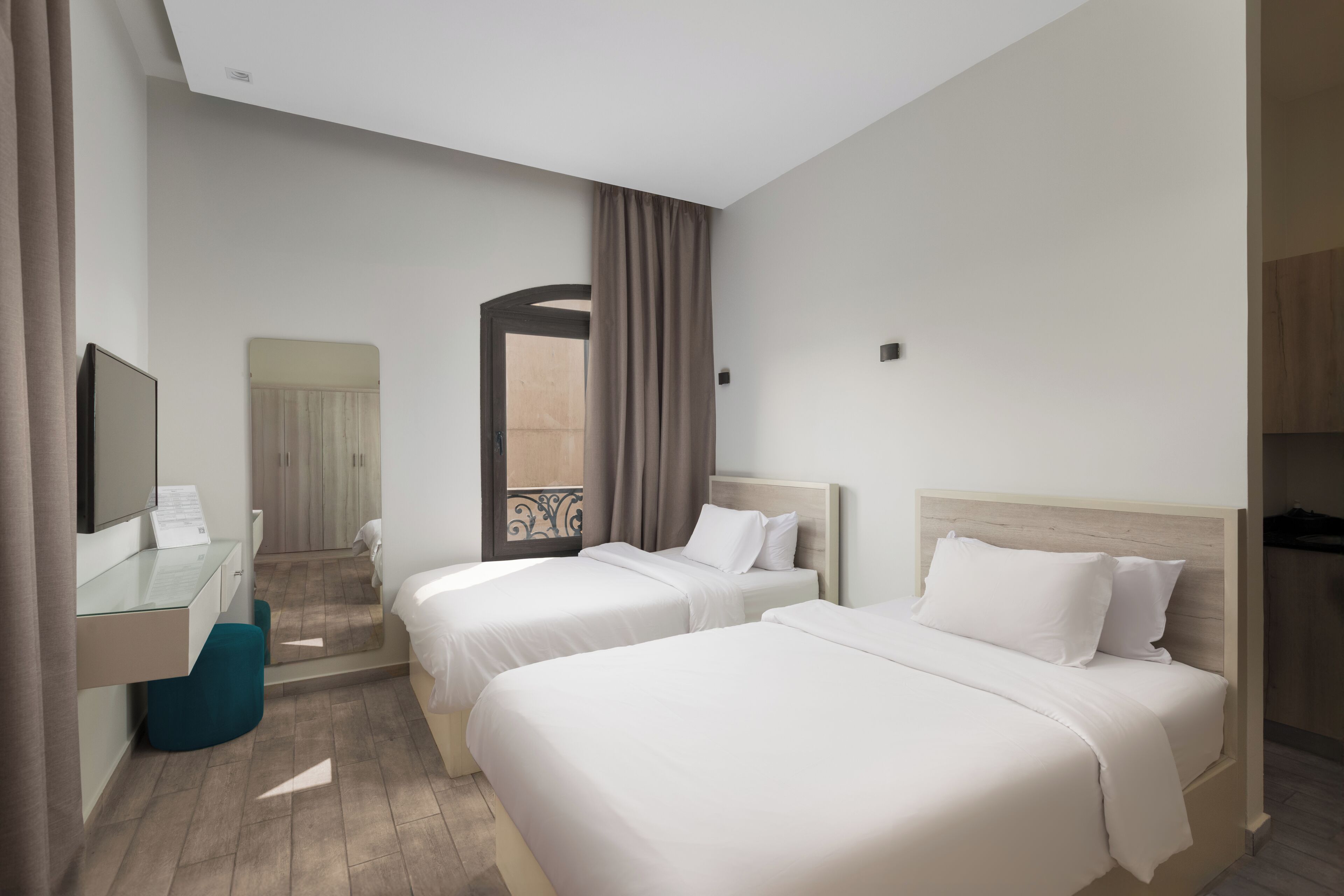 A hotel room with two beds, a desk, a TV, and a bathroom.