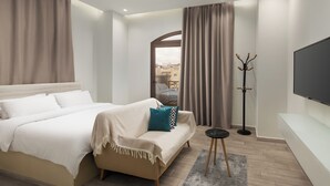 A hotel room with a bed, a sofa, a TV, a coat rack, and a view of buildings outside. - Sleep Inn Apart-hotel (New Cairo)