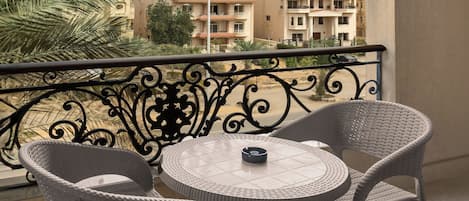 A balcony with two wicker chairs and a small round table, overlooking a residential area with buildings and a palm tree.